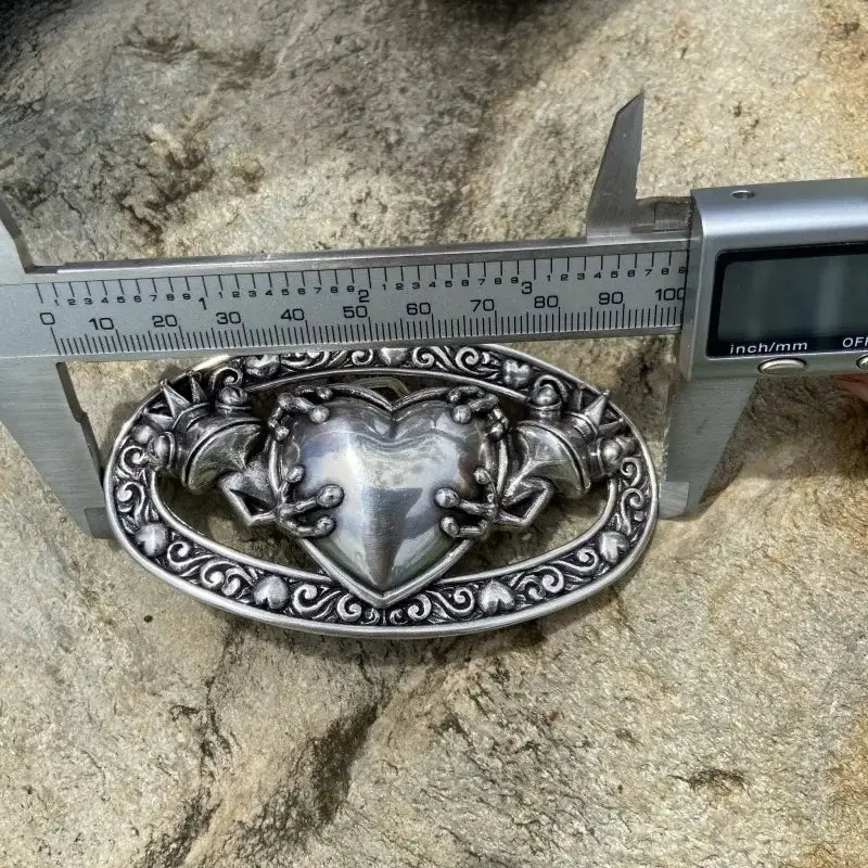 boucle de ceinture celtique grenouille en alliage métallique mesurée avec un réglet sur une pierre