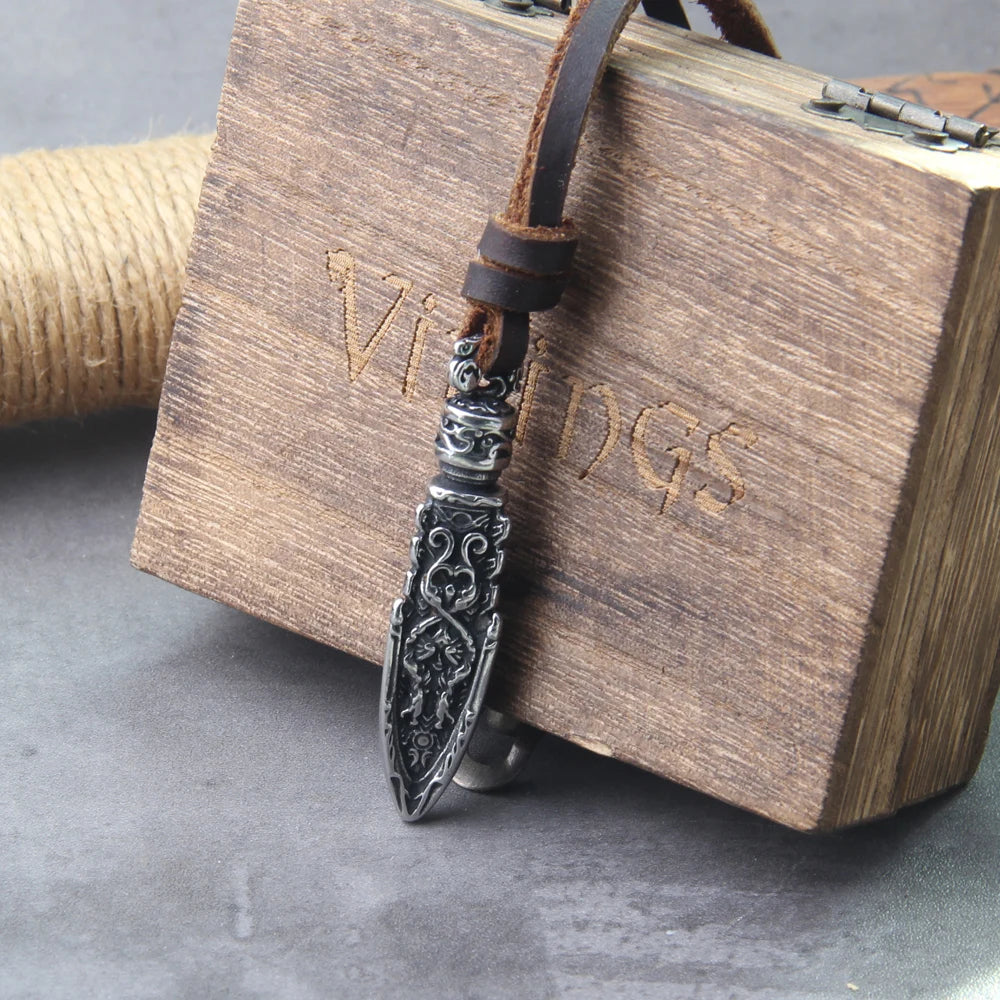 Celtic warrior arrowhead necklace on leather cord next to wooden box labeled 'Vikings'.