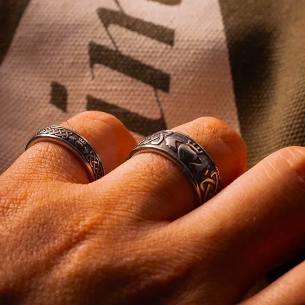 Deux bagues Claddagh en acier inoxydable sur une main, symbolisant l'amour et l'engagement, sur fond texturé.