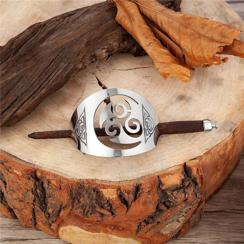Celtic metal and wood hair pin with triskel and knot design, displayed on a wooden surface with autumn leaves.
