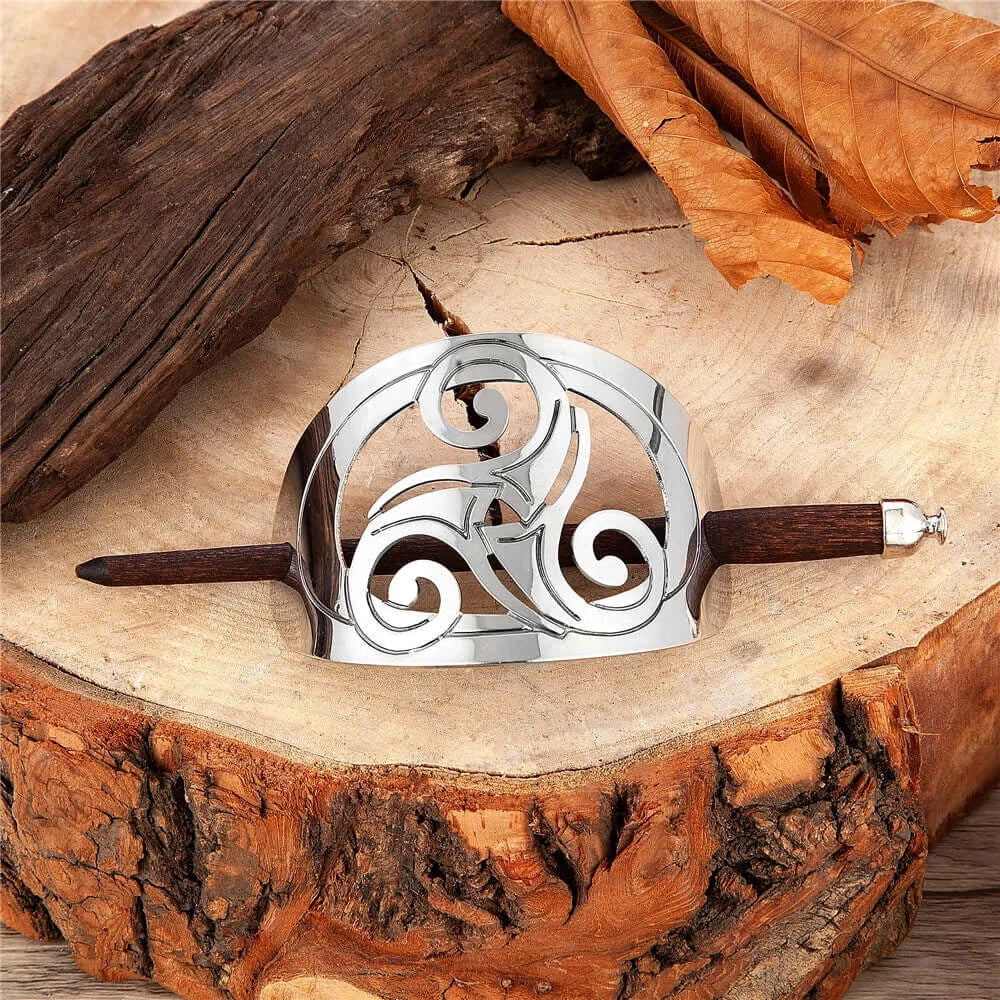 Celtic hairpin in metal and wood featuring intricate triskel and knot designs, placed on a rustic wooden surface.
