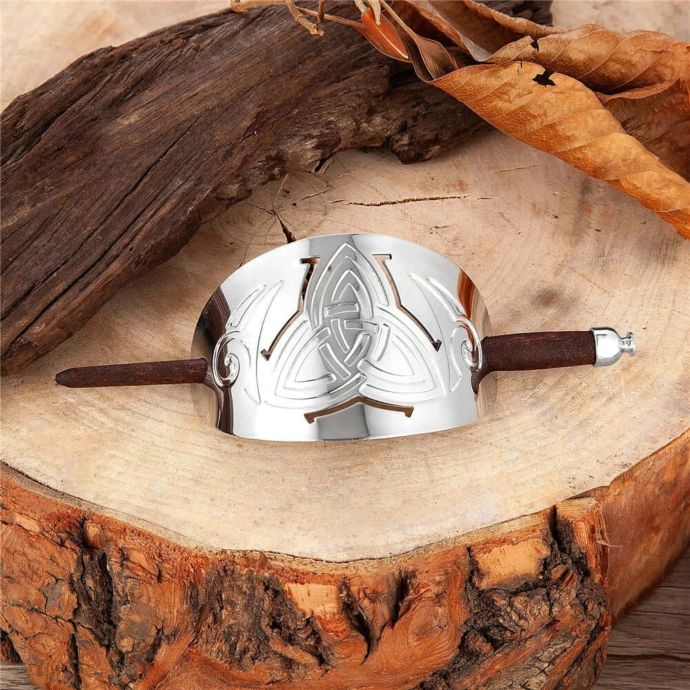 Celtic hairpin in metal and wood with triskel design on wooden background, elegant hair accessory.
