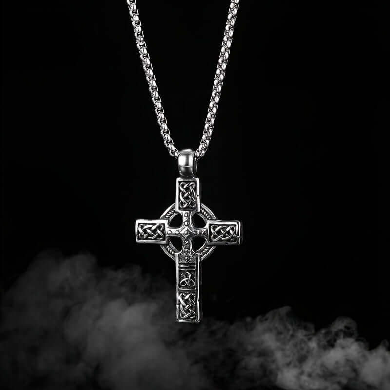 Pendentif croix celtique en acier inoxydable avec finition rustique sur un fond noir.
