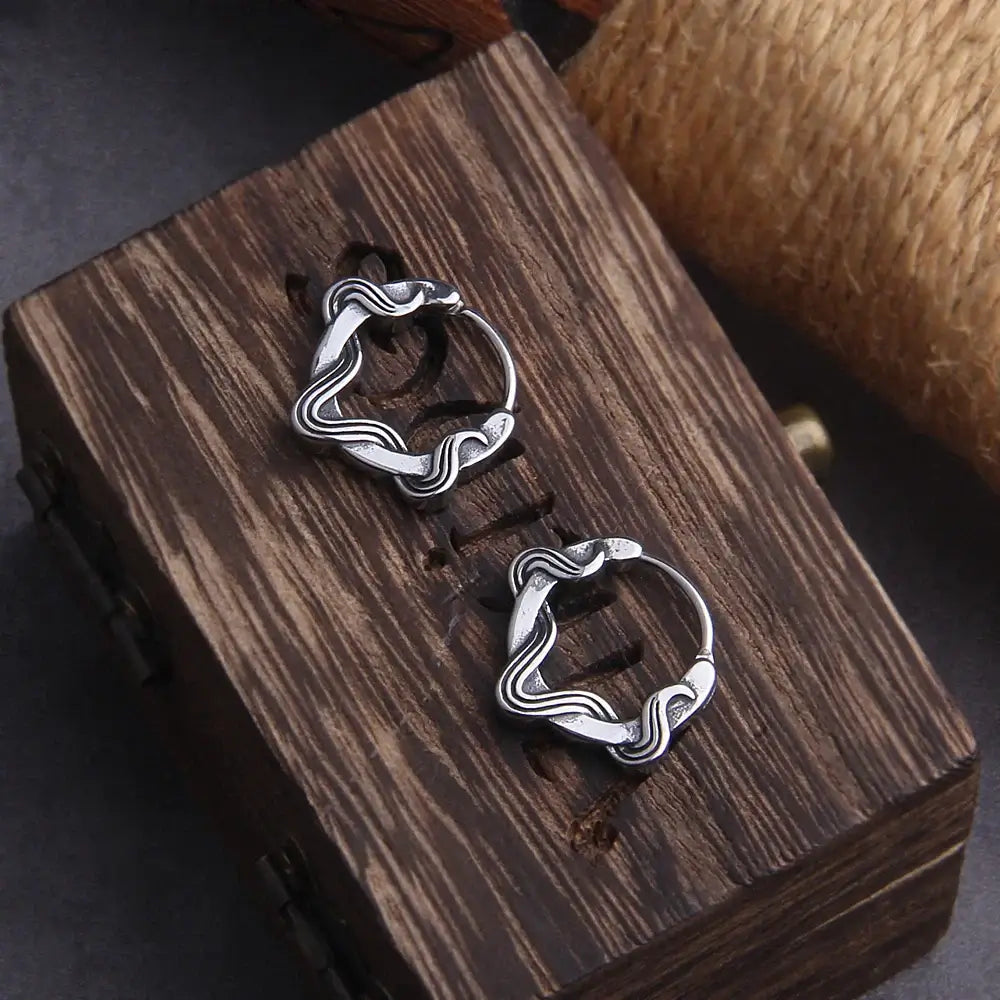 Elegant silver hoop earrings with a wavy design displayed on a wooden box.
