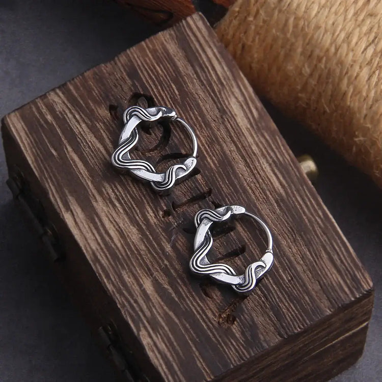 Elegant silver hoop earrings with a wavy design displayed on a wooden box.