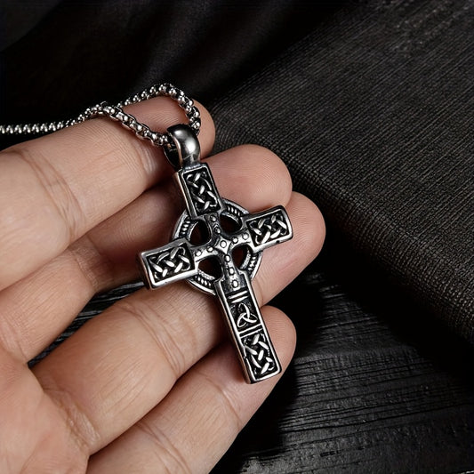 Pendentif croix celtique en acier inoxydable avec finition rustique, porté à la main sur un fond sombre.