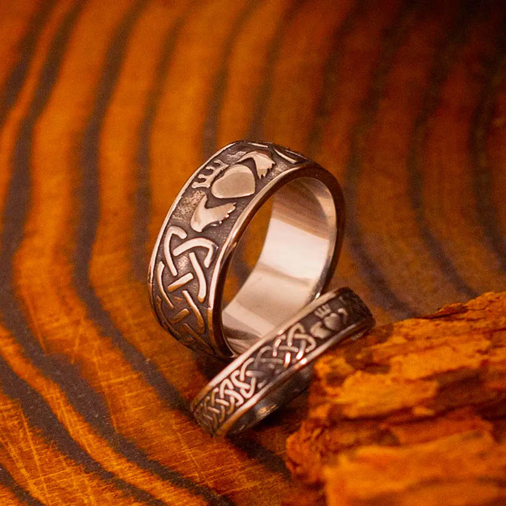 Bague Claddagh en acier inoxydable avec motifs celtique sur fond en bois naturel.