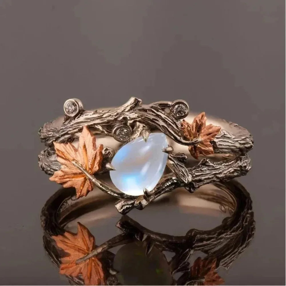 Bague branche d'arbre avec sa pierre  blanches ornée de feuilles et pierre précieuse sur fond sombre.